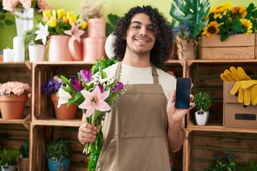 Poster - Hispanic man with curly hair working at florist shop showing smartphone screen smiling with a happy and cool smile on face. showing teeth.