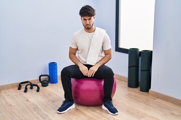 Canvas Print - Hispanic man with beard sitting on pilate balls at yoga room skeptic and nervous, frowning upset because of problem. negative person.