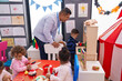 © Krakenimages.com - Hispanic man and group of kids playing with play kitchen standing at kindergarten