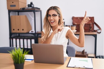 Sticker - Young blonde woman working at the office wearing glasses smiling and looking at the camera pointing with two hands and fingers to the side.