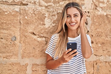 Sticker - Young blonde woman smiling confident using smartphone over isolated stone background