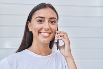 Wall Mural - Young beautiful hispanic woman smiling confident talking on the smartphone over isolated white background