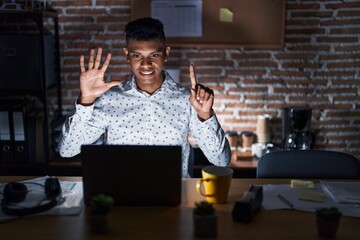 Wall Mural - Young hispanic man working at the office at night showing and pointing up with fingers number six while smiling confident and happy.