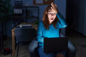 Canvas Print - Brunette woman working at the office at night surprised with hand on head for mistake, remember error. forgot, bad memory concept.