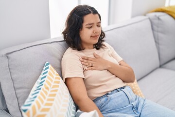 Sticker - Young woman sitting on sofa touching chest at home