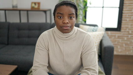 Wall Mural - African american woman sitting on sofa with serious expression at home