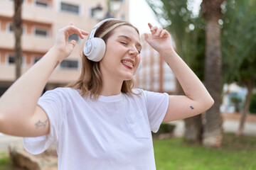  Young caucasian woman listening to music and dancing at park