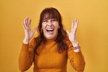 Canvas Print - Middle age hispanic woman standing over yellow background crazy and mad shouting and yelling with aggressive expression and arms raised. frustration concept.