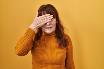 Sticker - Middle age hispanic woman standing over yellow background covering eyes with hand, looking serious and sad. sightless, hiding and rejection concept