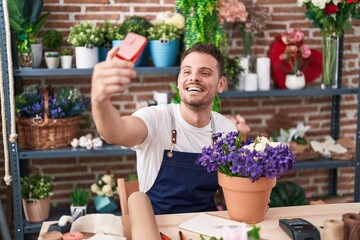 Sticker - Young hispanic man florist make selfie by smartphone sitting on table at florist