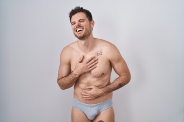 Wall Mural - Young hispanic man standing shirtless wearing underware smiling and laughing hard out loud because funny crazy joke with hands on body.