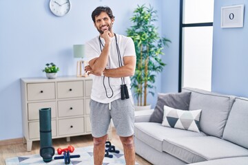 Canvas Print - Handsome latin man wearing sportswear at home looking confident at the camera smiling with crossed arms and hand raised on chin. thinking positive.