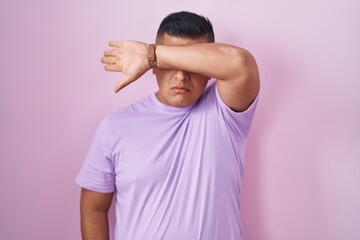 Canvas Print - Young hispanic man standing over pink background covering eyes with arm, looking serious and sad. sightless, hiding and rejection concept