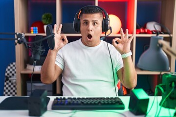 Canvas Print - Young hispanic man playing video games looking surprised and shocked doing ok approval symbol with fingers. crazy expression