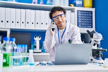 Sticker - Young hispanic man scientist using laptop talking on smartphone at laboratory