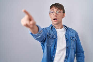 Sticker - Caucasian blond man standing wearing glasses pointing with finger surprised ahead, open mouth amazed expression, something on the front