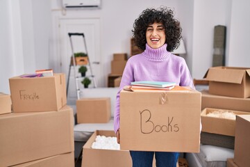 Wall Mural - Young brunette woman with curly hair moving to a new home holding cardboard box celebrating crazy and amazed for success with open eyes screaming excited.