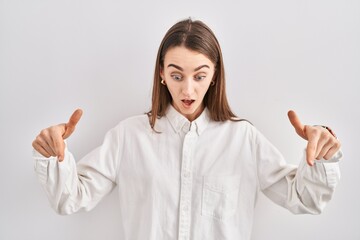 Poster - Young caucasian woman standing over isolated background pointing down with fingers showing advertisement, surprised face and open mouth