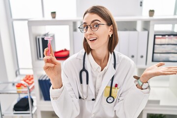 Canvas Print - Young caucasian doctor woman holding razor celebrating achievement with happy smile and winner expression with raised hand