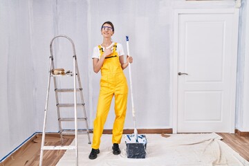 Sticker - Young caucasian woman painting walls cheerful with a smile on face pointing with hand and finger up to the side with happy and natural expression