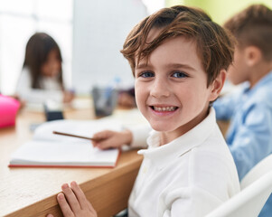 Canvas Print - Adorable caucasian boy student writing on notebook studying at classroom