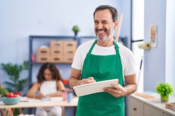 Poster - Middle age hispanic man painting on art notebook with pencils winking looking at the camera with sexy expression, cheerful and happy face.