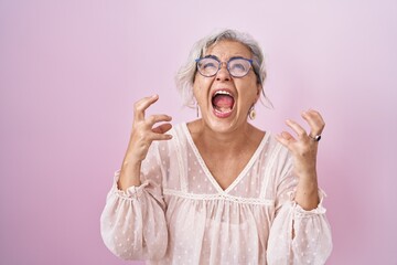 Sticker - Middle age woman with grey hair standing over pink background crazy and mad shouting and yelling with aggressive expression and arms raised. frustration concept.