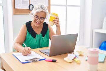 Poster - Middle age grey-haired woman business worker writing on document drinking coffee at office