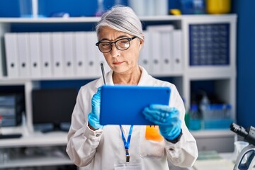 Middle age grey-haired woman scientist using touchpad working at laboratory