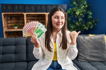 Sticker - Young latin woman holding norwegian money pointing thumb up to the side smiling happy with open mouth