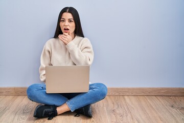 Poster - Young woman using laptop sitting on the floor at home looking fascinated with disbelief, surprise and amazed expression with hands on chin