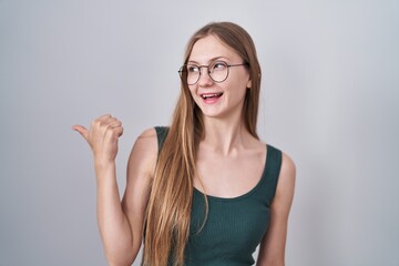 Canvas Print - Young caucasian woman standing over white background smiling with happy face looking and pointing to the side with thumb up.