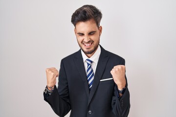 Poster - Young hispanic man with tattoos wearing business suit and tie very happy and excited doing winner gesture with arms raised, smiling and screaming for success. celebration concept.