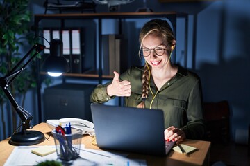 Canvas Print - Young blonde woman working at the office at night doing happy thumbs up gesture with hand. approving expression looking at the camera showing success.