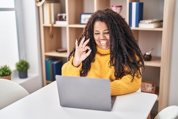 Poster - Plus size hispanic woman using laptop at home doing ok sign with fingers, smiling friendly gesturing excellent symbol