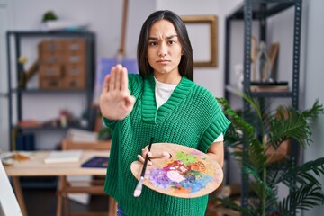 Wall Mural - Young south asian woman holding painter palette with open hand doing stop sign with serious and confident expression, defense gesture