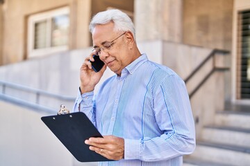 Canvas Print - Senior man talking on the smartphone reading document at street