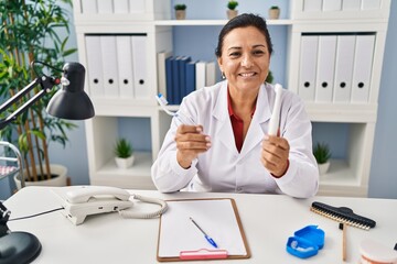 Poster - Middle age hispanic woman dentist holding toothbrushes at clinic