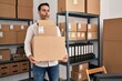 Young hispanic man with beard working at small business ecommerce holding delivery boxes making fish face with mouth and squinting eyes, crazy and comical.