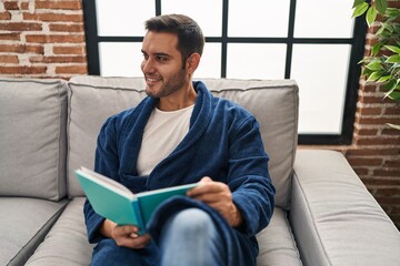 Sticker - Young hispanic man wearing bathrobe reading book at home