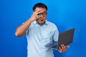 Sticker - Chinese young man using computer laptop peeking in shock covering face and eyes with hand, looking through fingers with embarrassed expression.