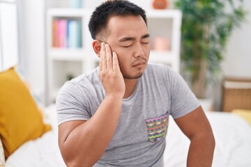 Poster - Young chinese man suffering for ear pain sitting on bed at bedroom