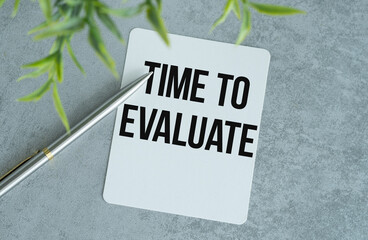 Time to Evaluate word with Notepad and green plant on gray background.