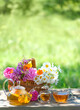 flowers in basket, glass teapot and cups with herbal tea on table, natural abstract background. summer season. Beautiful rustic composition. relax time. useful calming tea. Tea party in garden
