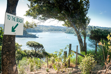 Sticker - Sign with words to the beach and arrow fixed to tree at top of cliff and view across picturesque bay