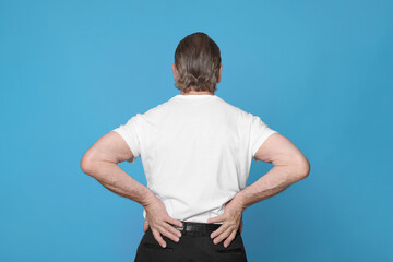 Wall Mural - Senior man suffering from pain in back on light blue background. Arthritis symptoms