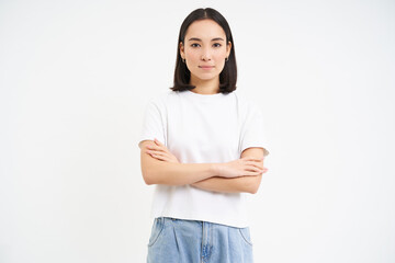 Wall Mural - Portrait of asian woman looks with confidence, cross arms on chest, stands in power pose, self-assured, stands over white background