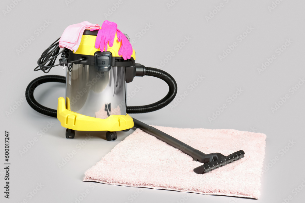 Vacuum cleaner with supplies and carpet on grey background