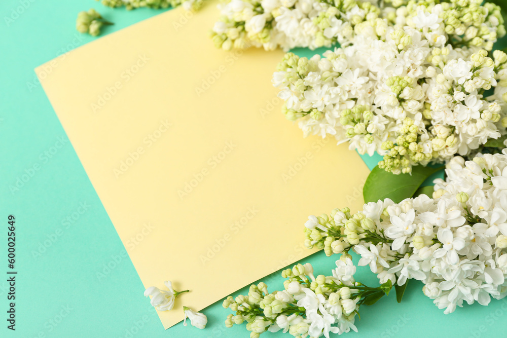 Yellow blank card and lilac flowers on turquoise background