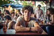 © wetzkaz - a young adult male or teenager outside in a cafe or bar, alone, gloomy or introverted or sad alone, fictional location. Generative AI